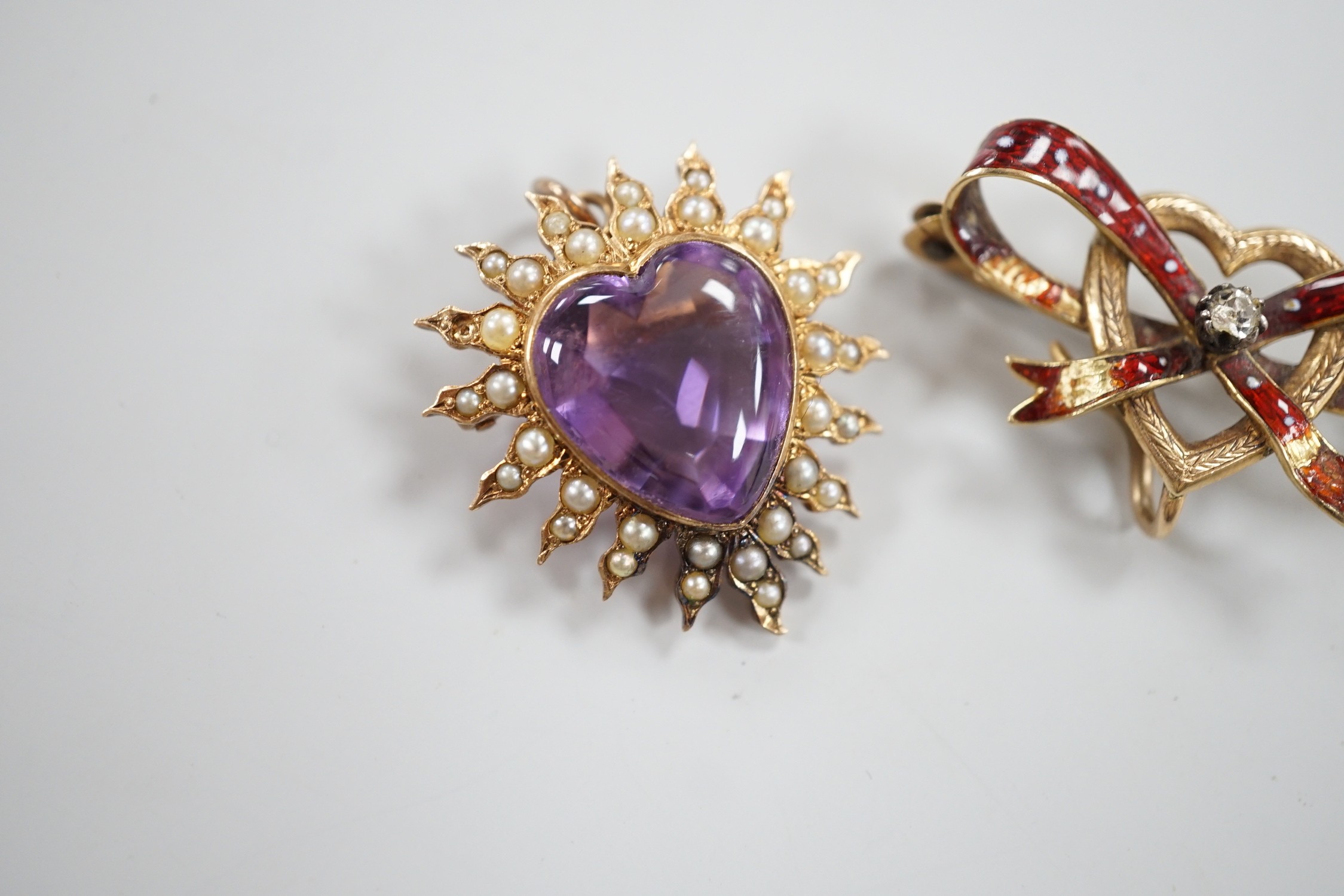 An early 20th century yellow metal amethyst and seed peart set heart shaped pendant brooch, 25mm, gross 5.3 grams and a yellow metal and enamel set ribbon bow and heart brooch (enamel a.f.).